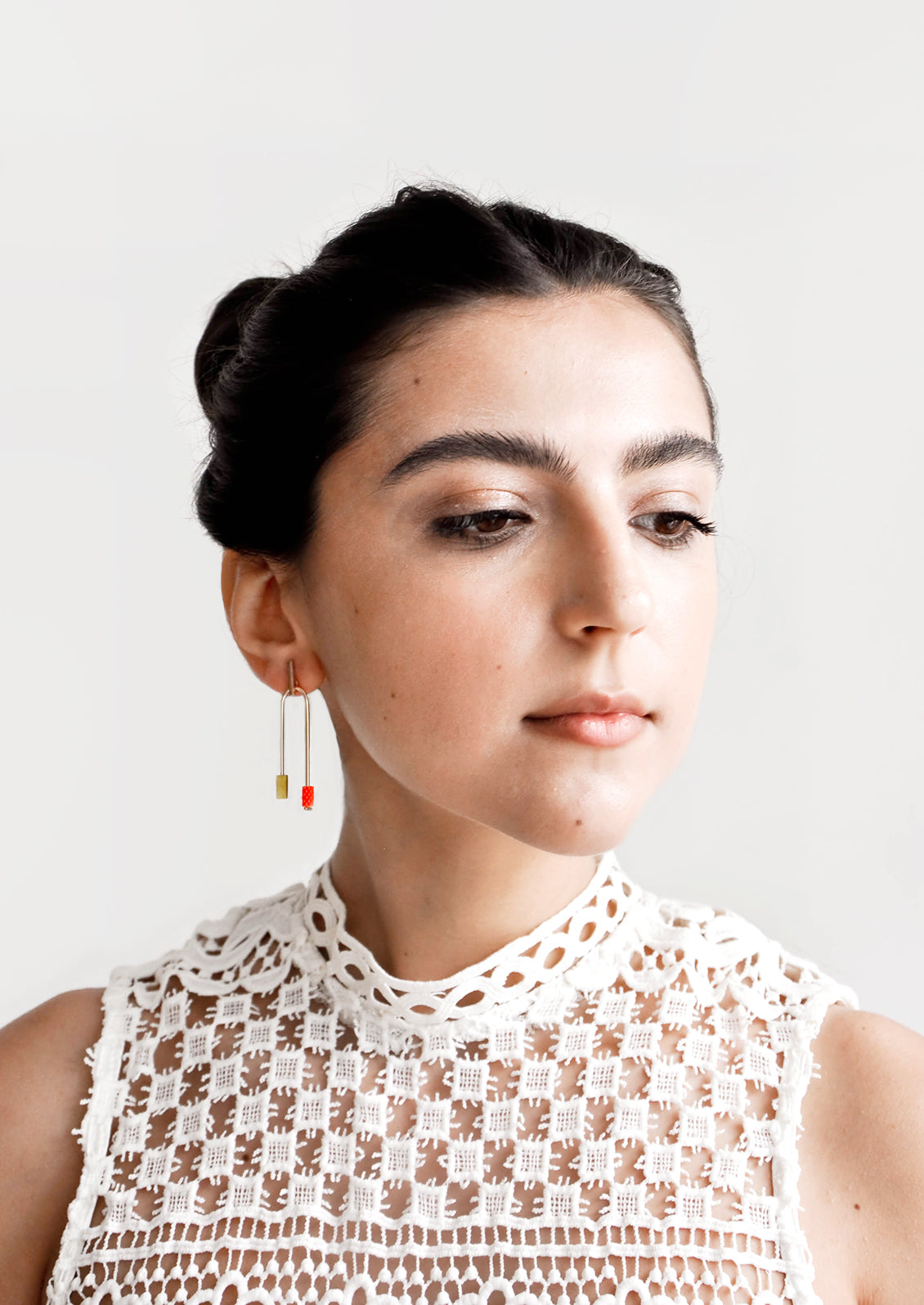 Model wears arced earrings and white blouse.