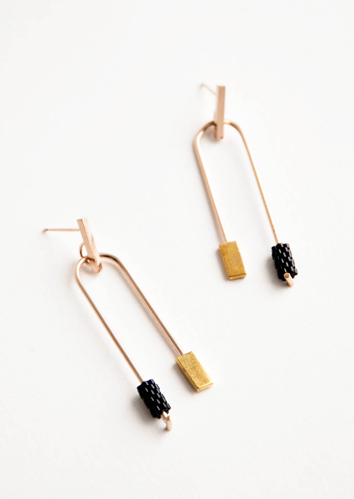 Post back gold earrings with curved arc featuring one black beaded end and one square gold end.