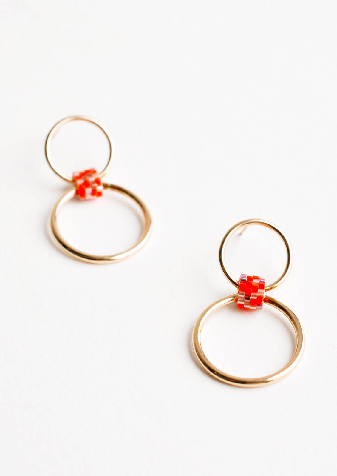 Post back earrings of one small gold hoop and one larger gold hoop connected by a loop of orange glass beads.