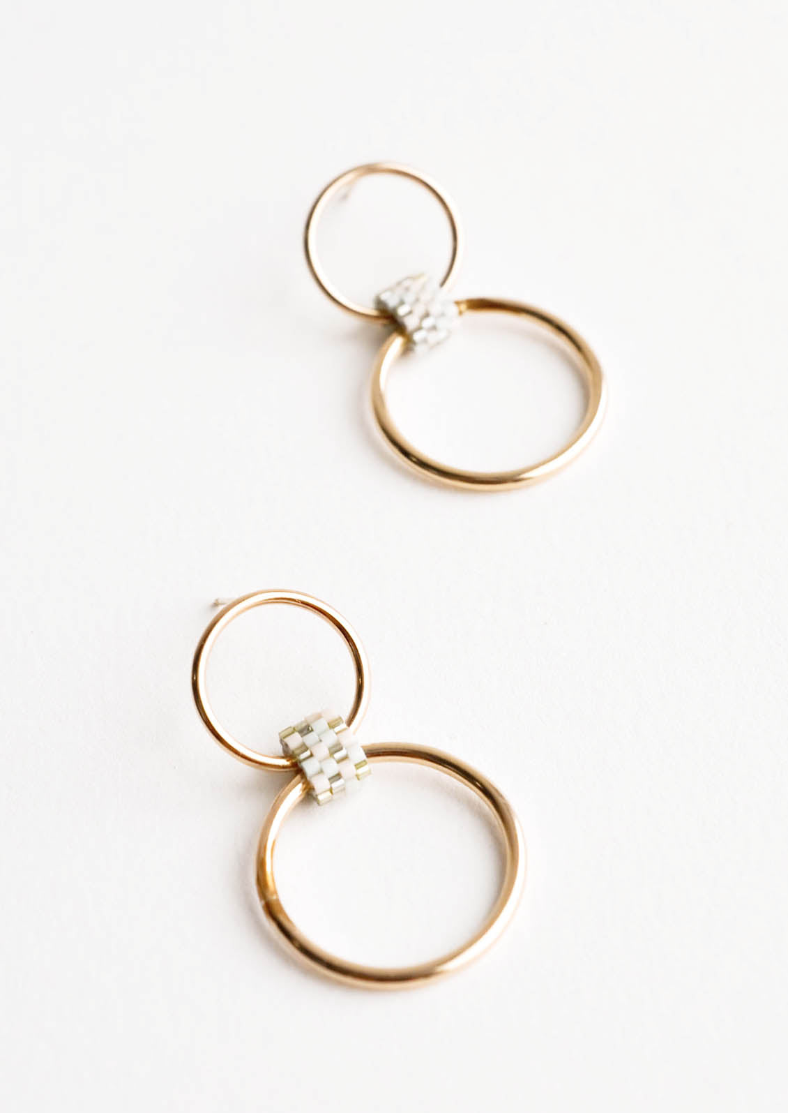 Post back earrings of one small hoop and one larger hoop connected by a loop of cream colored glass beads.