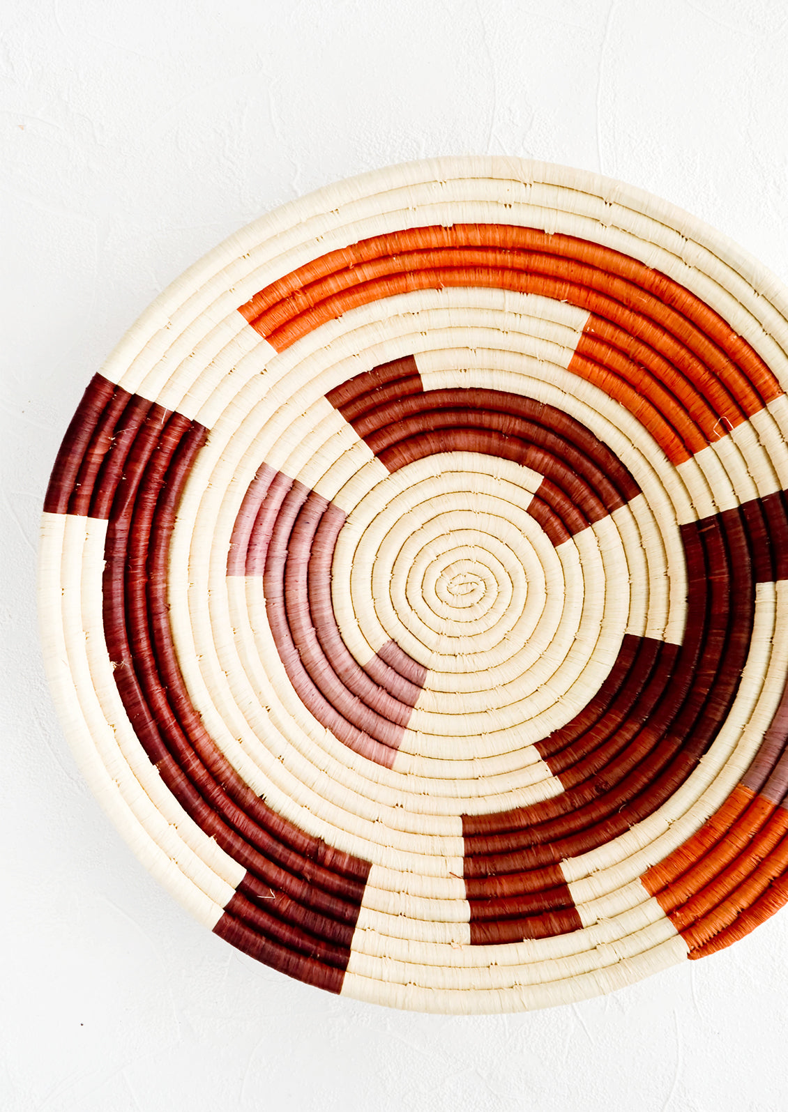 Round woven raffia bowl with interlocking, maze-like pattern in mauve, wine and orange
