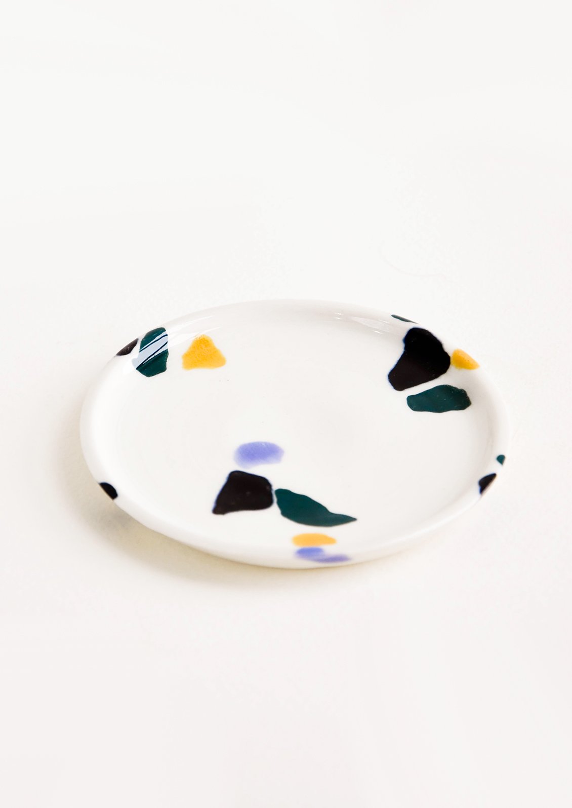 Small, plate-like ceramic dish in ivory with hand-painted, fragmented pattern in a mix of colors