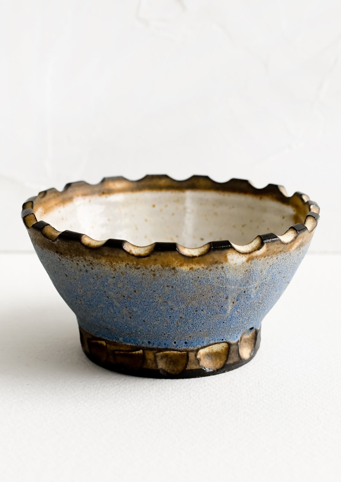 A ceramic bowl with carved notch rim in blue and brown.