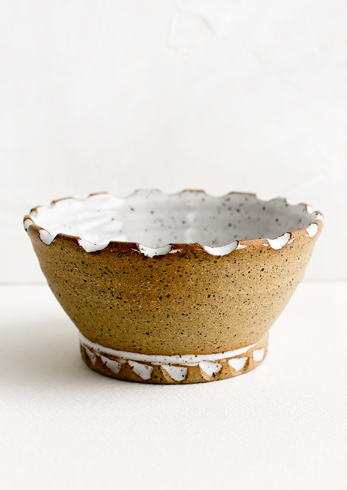 A ceramic bowl with carved notch rim in natural clay and white glaze.