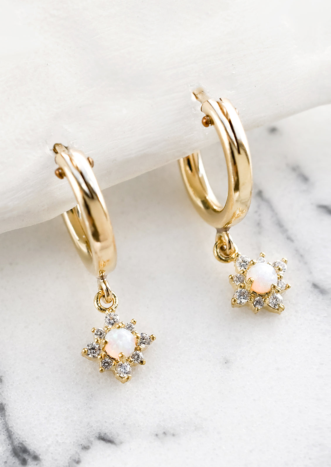 Gold huggie hoop earrings with crystal and opal north star charms.