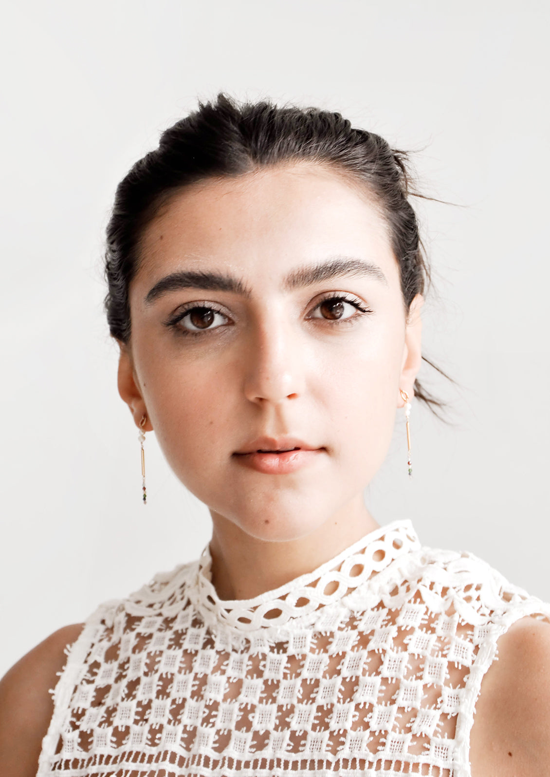 Model shot of a woman wearing earrings and a white top.