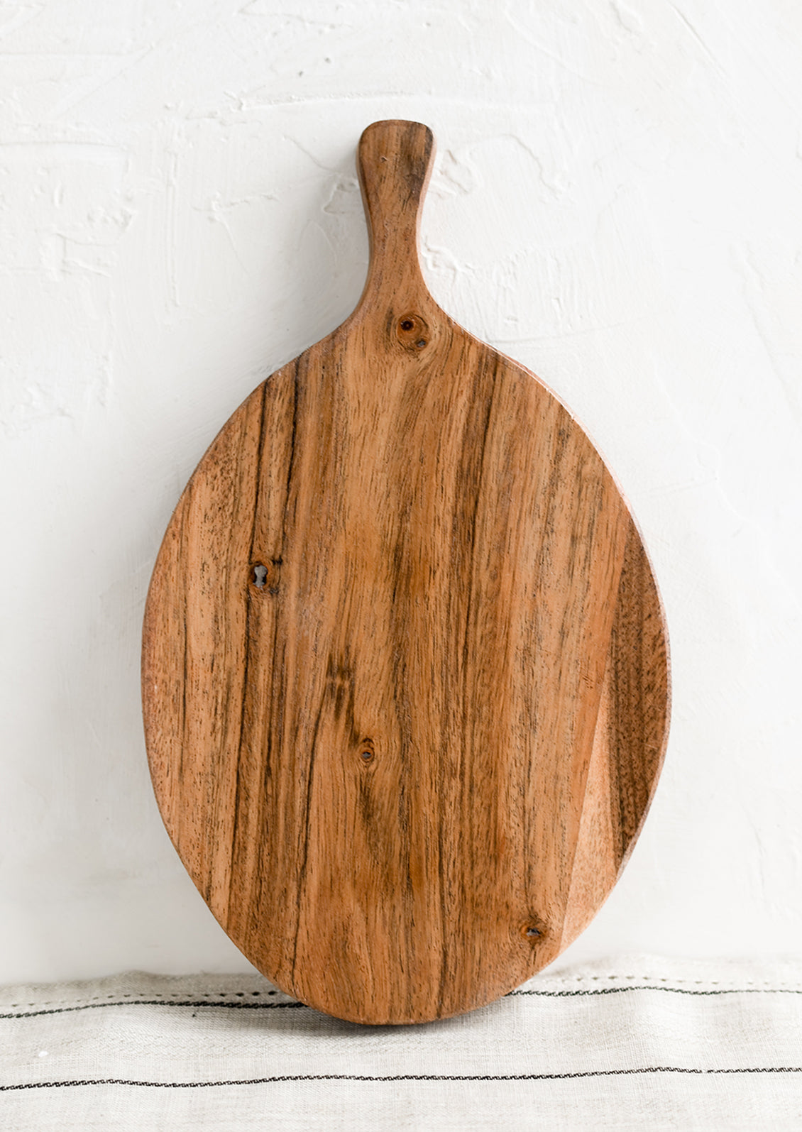 An oval shaped paddle-style cutting board in acacia wood.