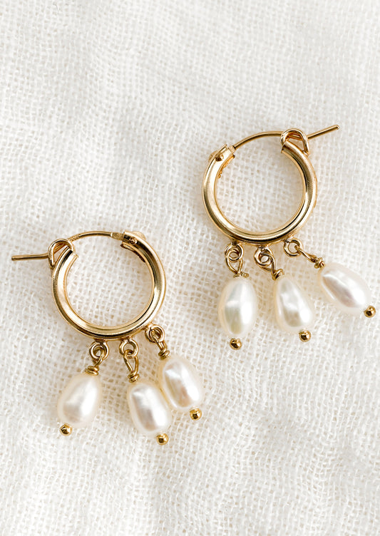 A pair of gold hoop earrings with three dangling pearls on each.