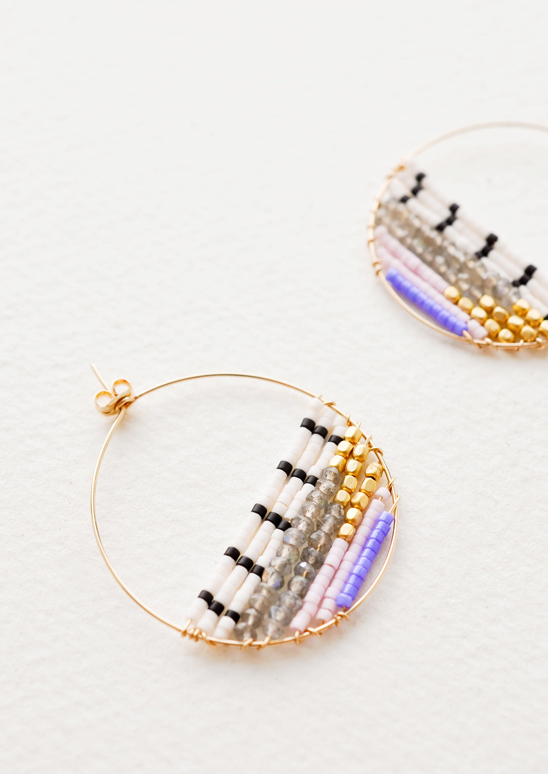 Close up of delicate gold hoop with multi-colored beads filling bottom half of hoop. 