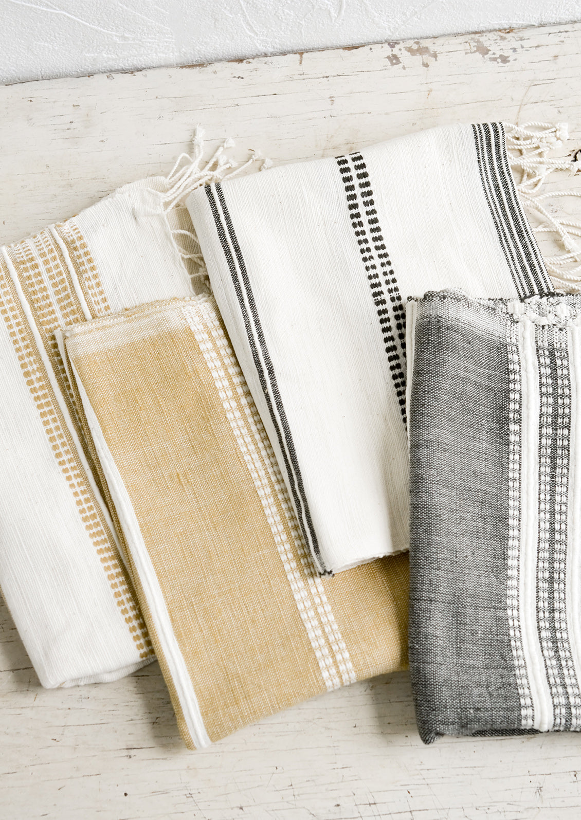 Four folded hand towels in natural, brown and black tones.