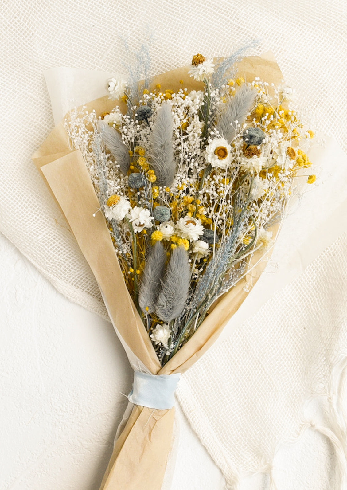 A large bouquet of dried yellow, white and light blue flowers wrapped in parchment paper