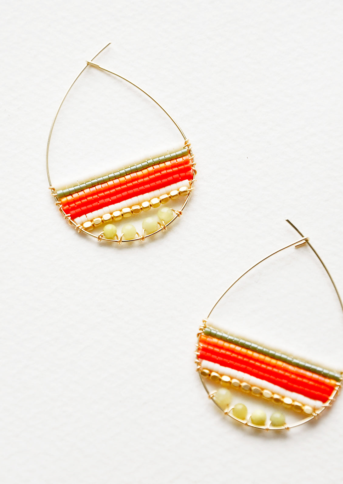 Teardrop shaped hoop earrings in yellow gold with multicolored yellow and red beaded bars across. 