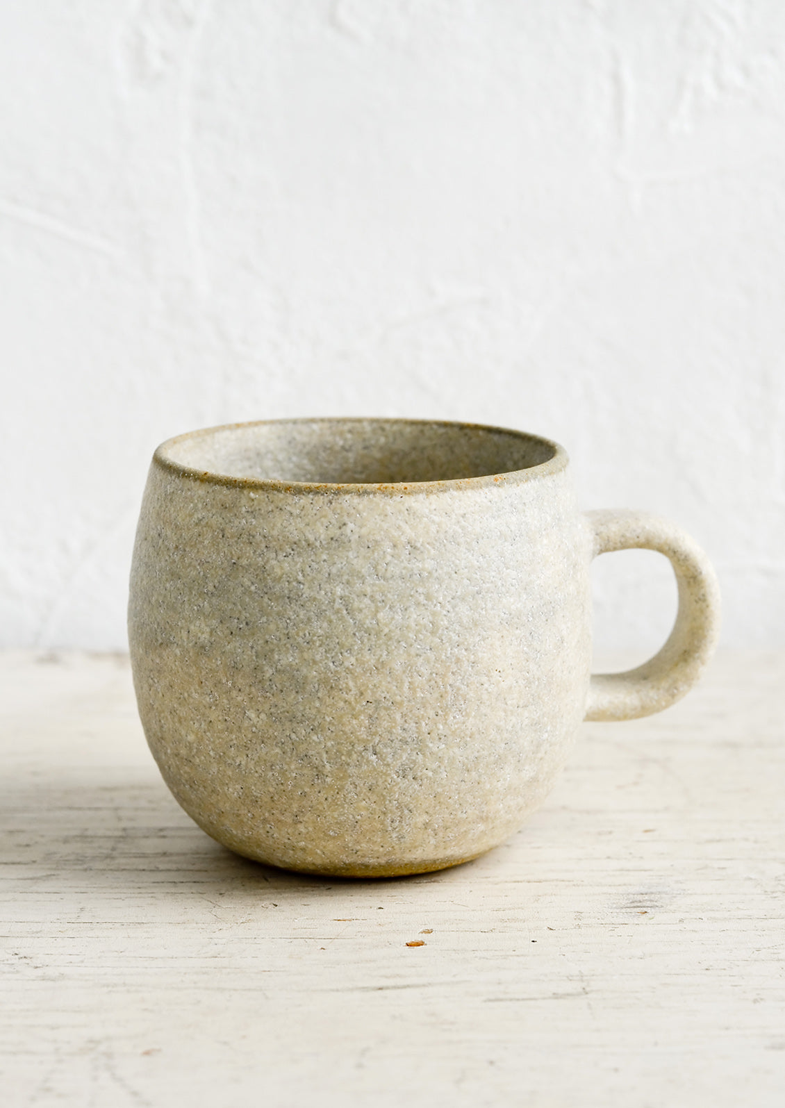 A ceramic coffee mug in a rustic, textured sandy glaze.