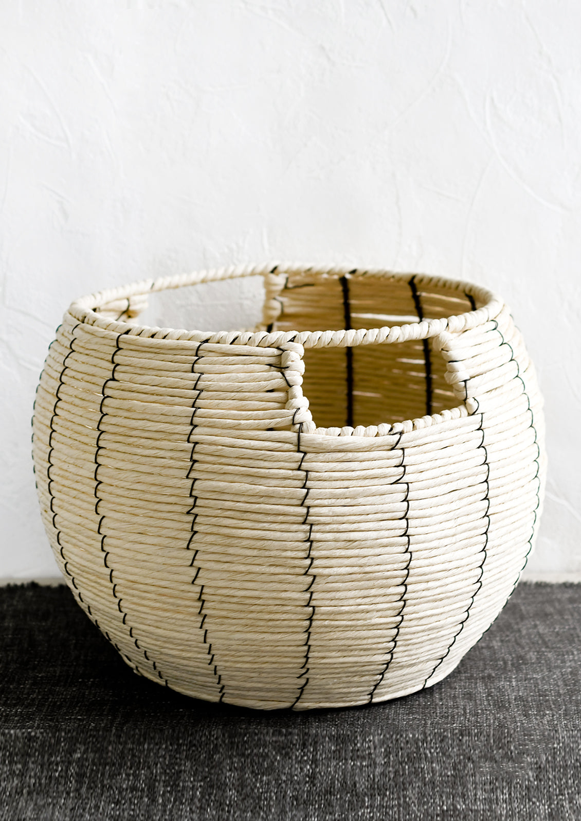 A round belly shaped basket in natural cord with thin black vertical stripe.