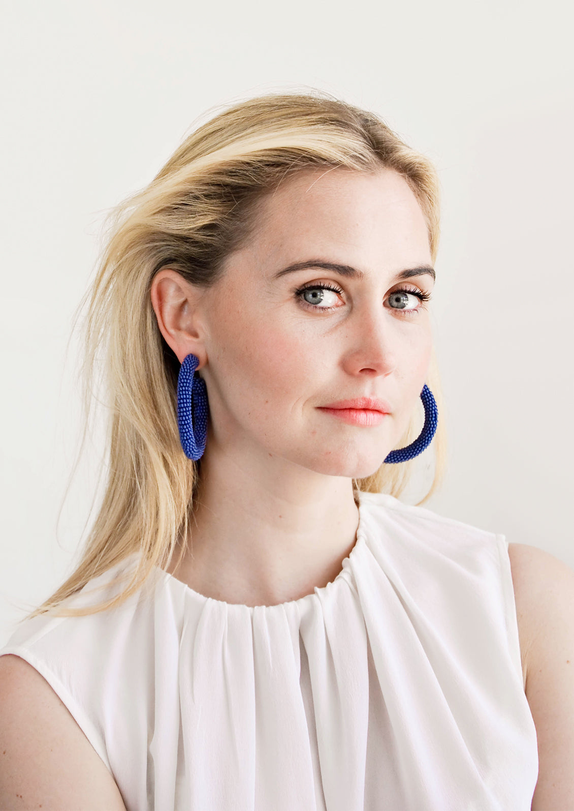 Model wears blue beaded hoop earrings and white blouse.