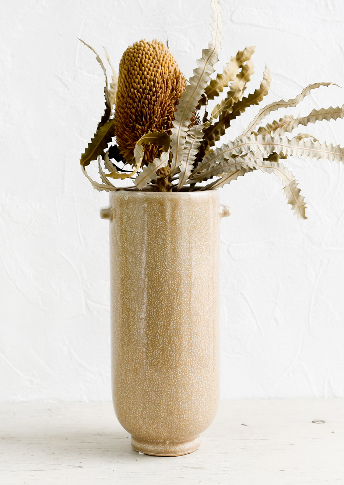 A tall brown ceramic vase with dried protea flower.