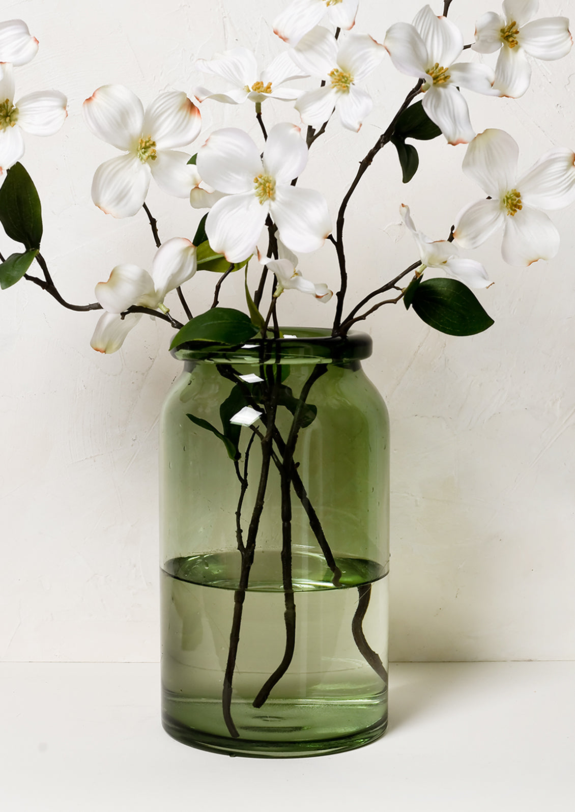 A tall green glass vase with dogwood branches.