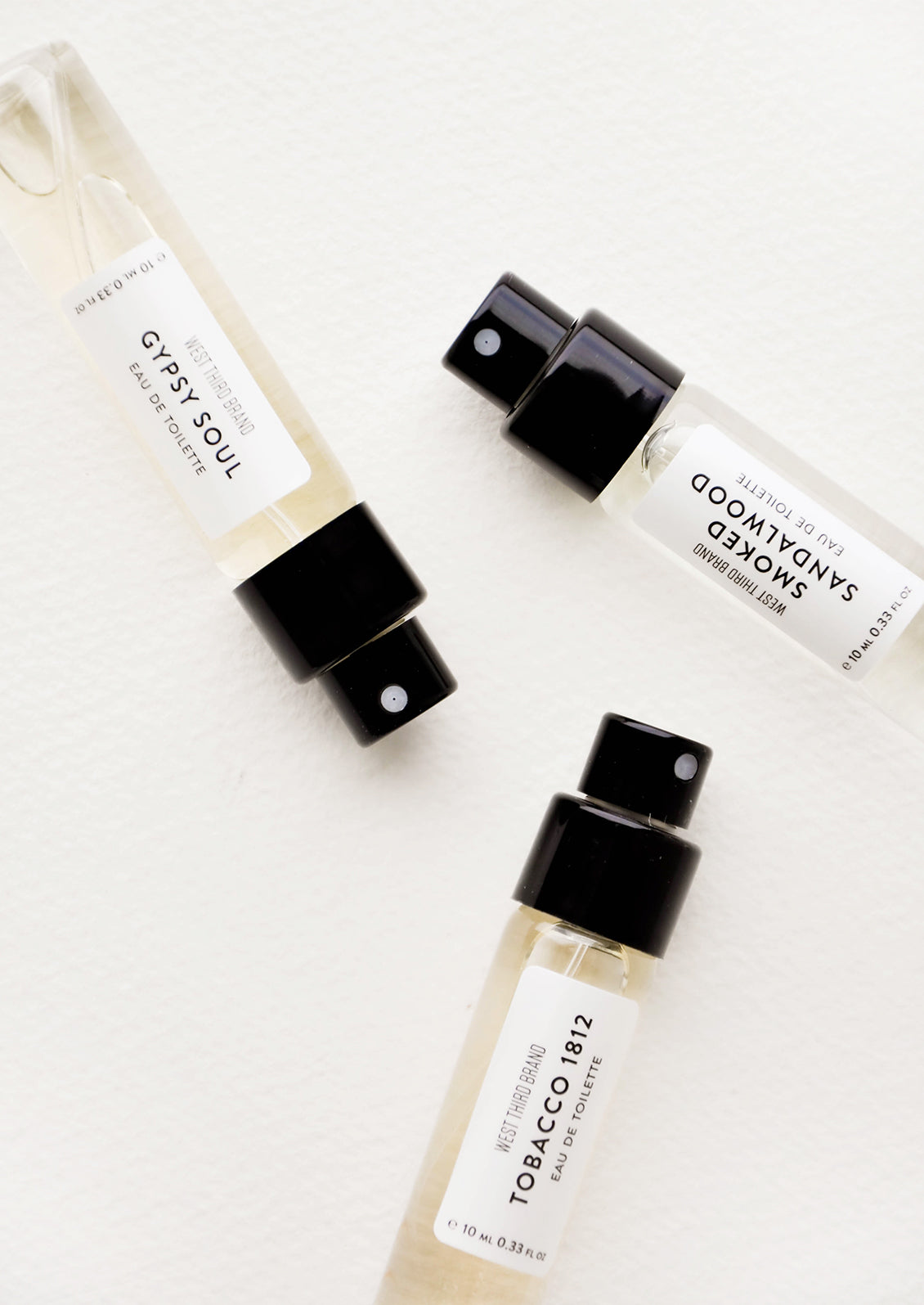 Three small perfume spray bottles with black spay caps and white labels with black text.