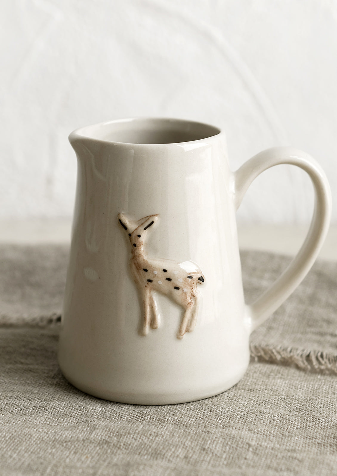 A small creamer pitcher in natural ivory with deer motif.