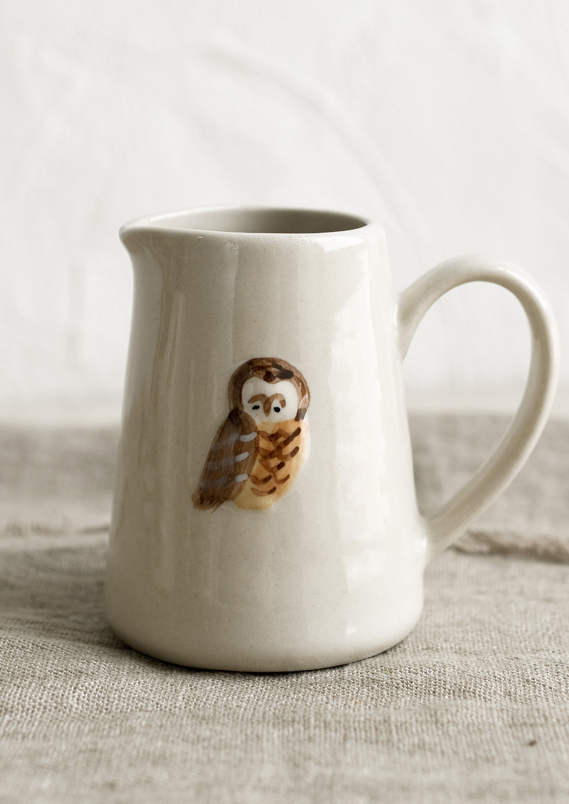 A small creamer pitcher in natural ivory with owl motif.