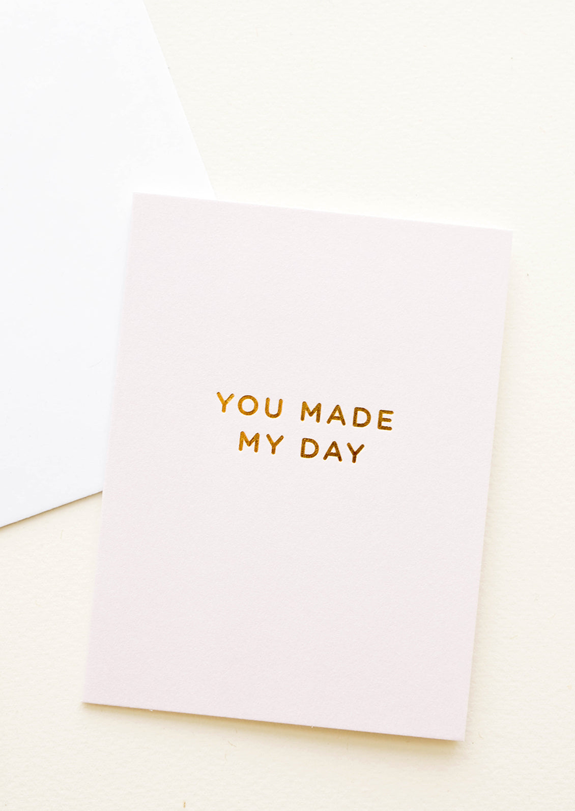 A white envelope and a light tan greeting card with the words "you made my day" in gold foil. 