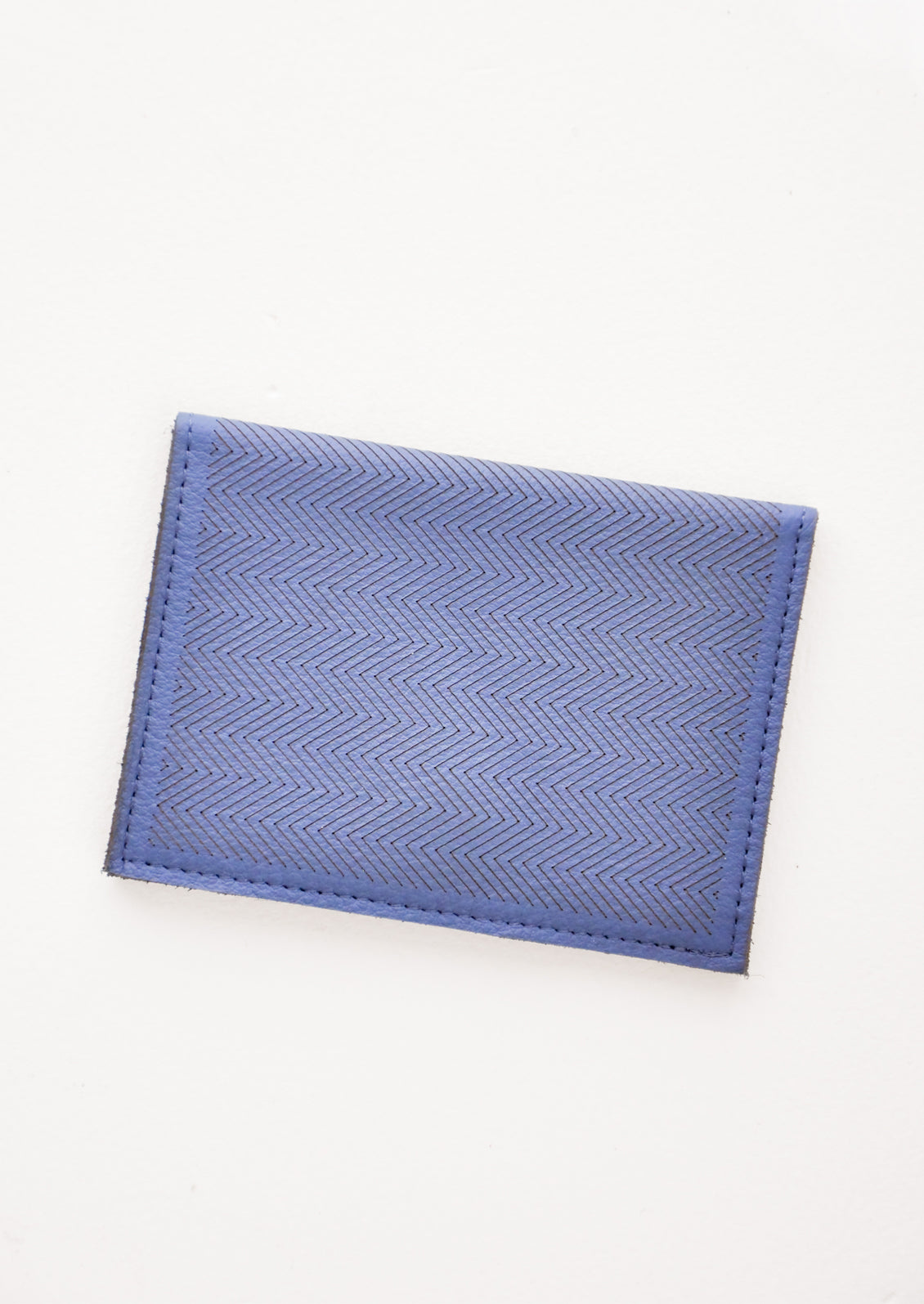 Slim dark blue leather wallet with two interior slip pockets that folds closed with a snap, shown closed with zig zag etched pattern. 